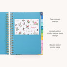 The 2025-2026 Spiral Daily Simplified Planner - Faraway Land by Simplified features a colorful floral design on the right page with YAY, YAY, and launch DAY text, and the left page has gold foil details with a text box announcing it as the Simplified Planner: Artist Edition.