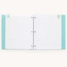 An open scrapbook with blank pages inside a mint, polka-dotted cover. This minimalistic Baby Book - Mint by Simplified features celebrate! at the bottom with silver rings binding the guided writing pages for memories.