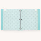 The open Baby Book - Mint by Simplified features light blue pages with small anchor patterns held by visible rings and topped with cute bookmarks. Its plain off-white background creates an ideal guided writing space.
