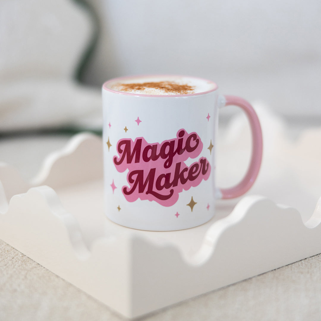 The Simplified “Mug - Magic Maker” is an 11 oz ceramic mug with a pink handle, bold pink lettering, and gold and pink stars. Microwave safe and ideal for lattes, it brings charm to your favorite drinks.