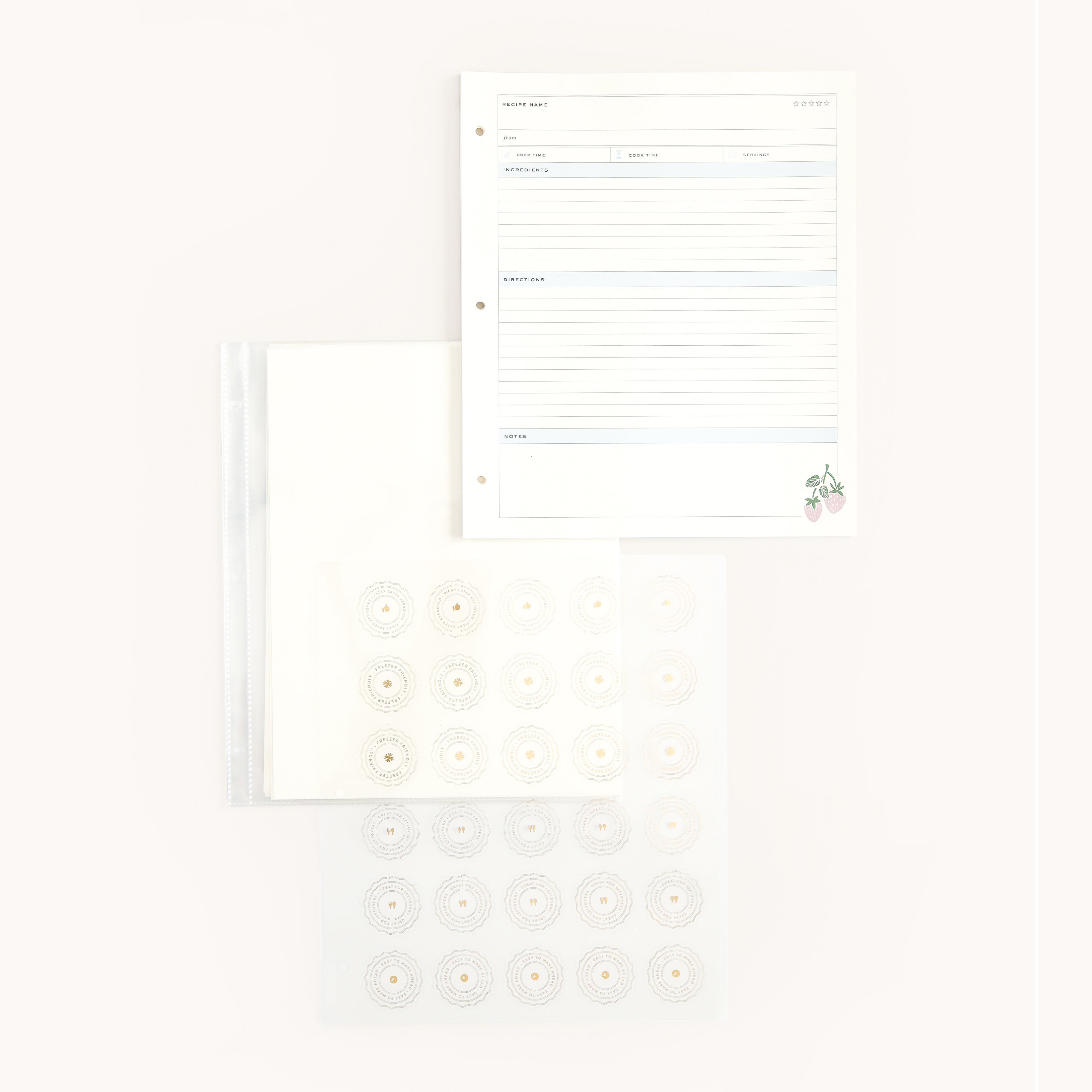 Overhead view of the Recipe Binder Page Pack by Simplified, featuring a lined sheet with floral illustrations, a transparent pocket, and recipe pages with circular patterns. The stationery set is artfully arranged on a light background.