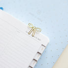 A Simplified Paper Clips - Bows securely holds a planner corner open, showing lined pages and tabbed dividers atop a pale blue polka-dotted surface.