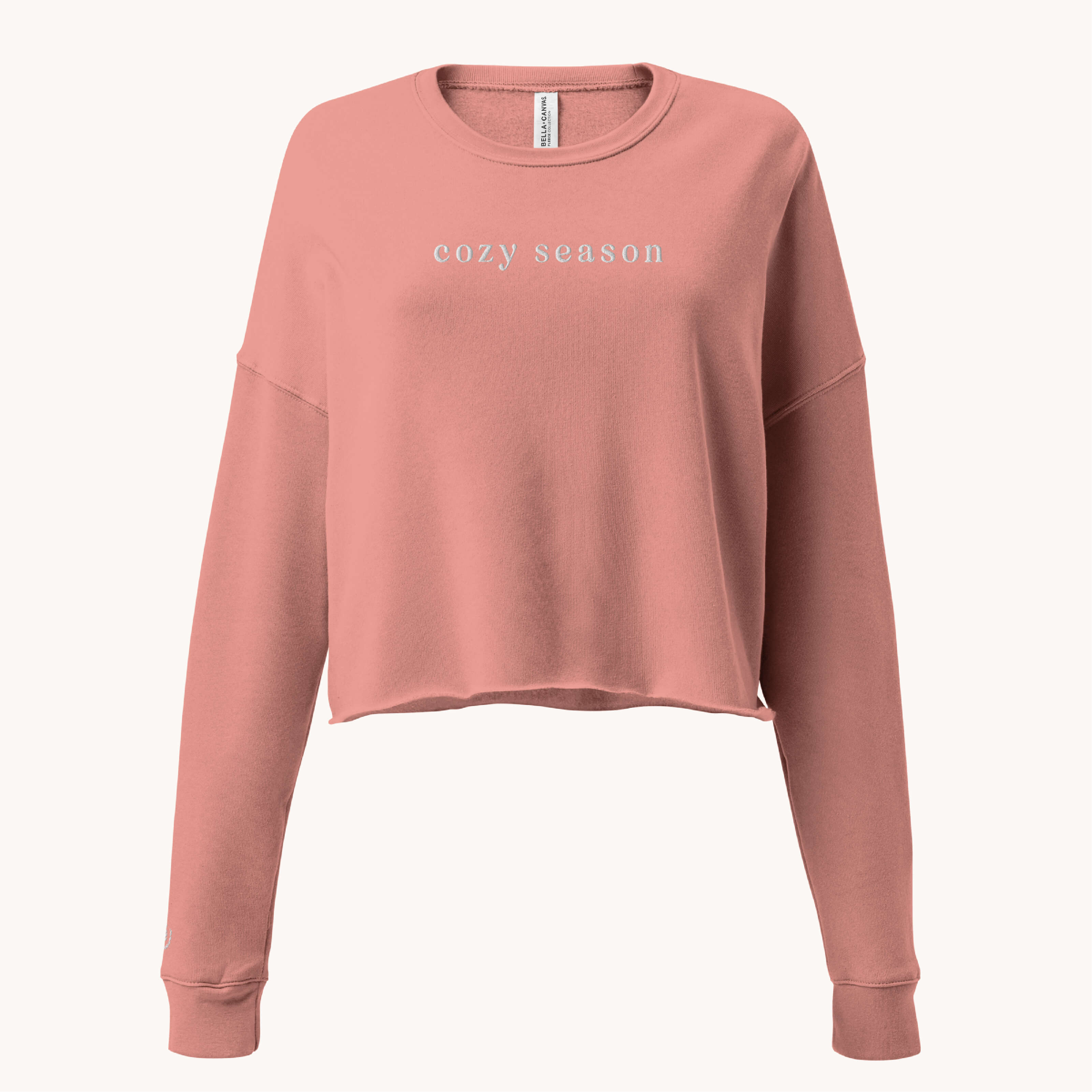 The Simplified Embroidered Crop Sweatshirt - Cozy Season features a mauve color, long sleeves, and white "cozy season" embroidery centered on the chest. Shown against a plain off-white background.