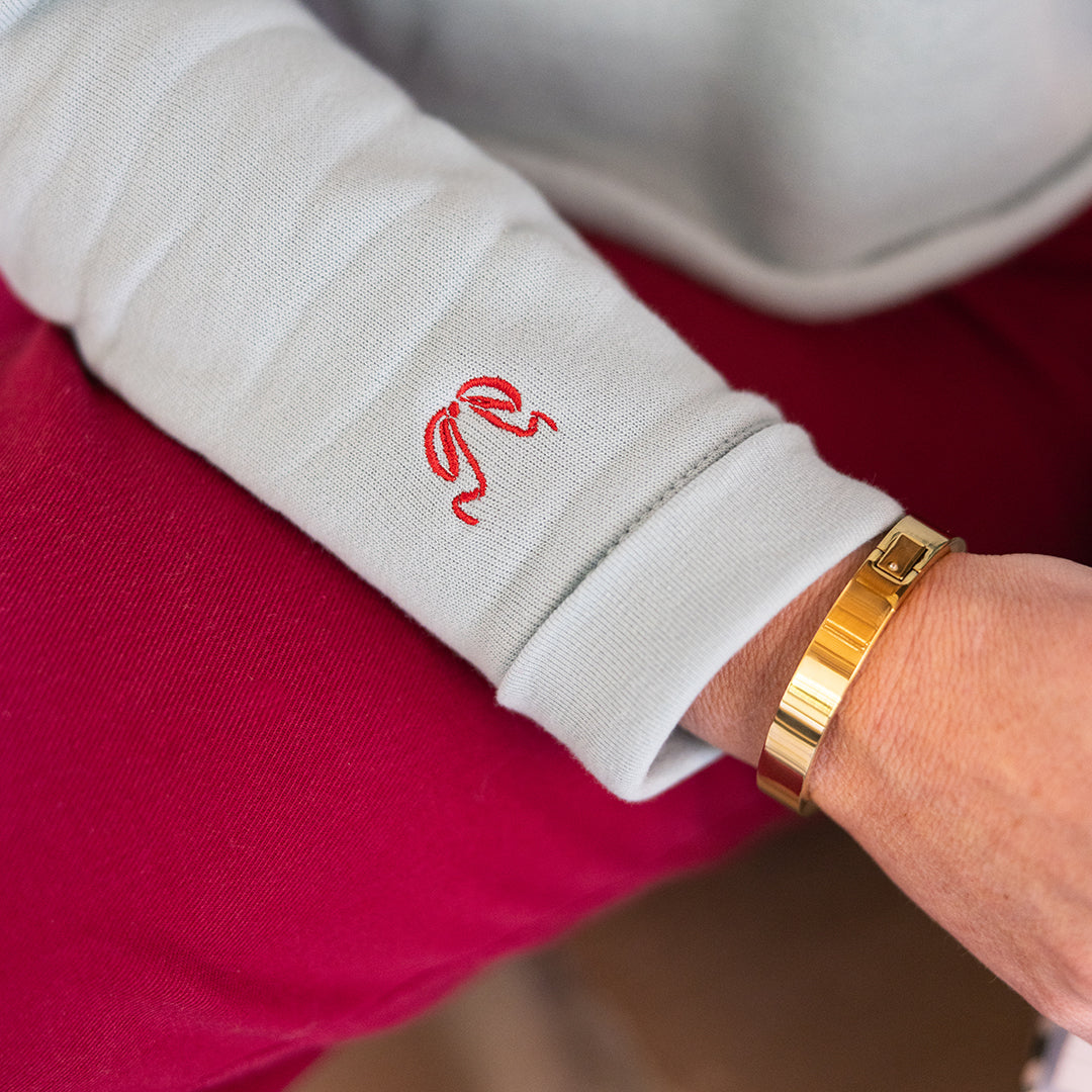 Wearing the Simplified Embroidered Crop Sweatshirt - Red Bow with red cuff detailing and matching red pants, accessorized with a gold bracelet.