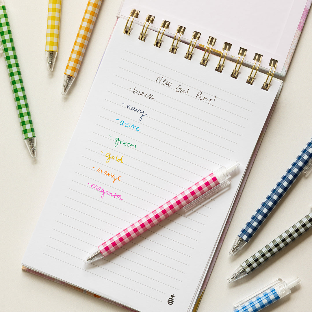 A Simplified Gel Pen Set - Gingham in coordinating colors is scattered around a notebook listing each gel pen color, all on a white surface with an elegant ivory box.