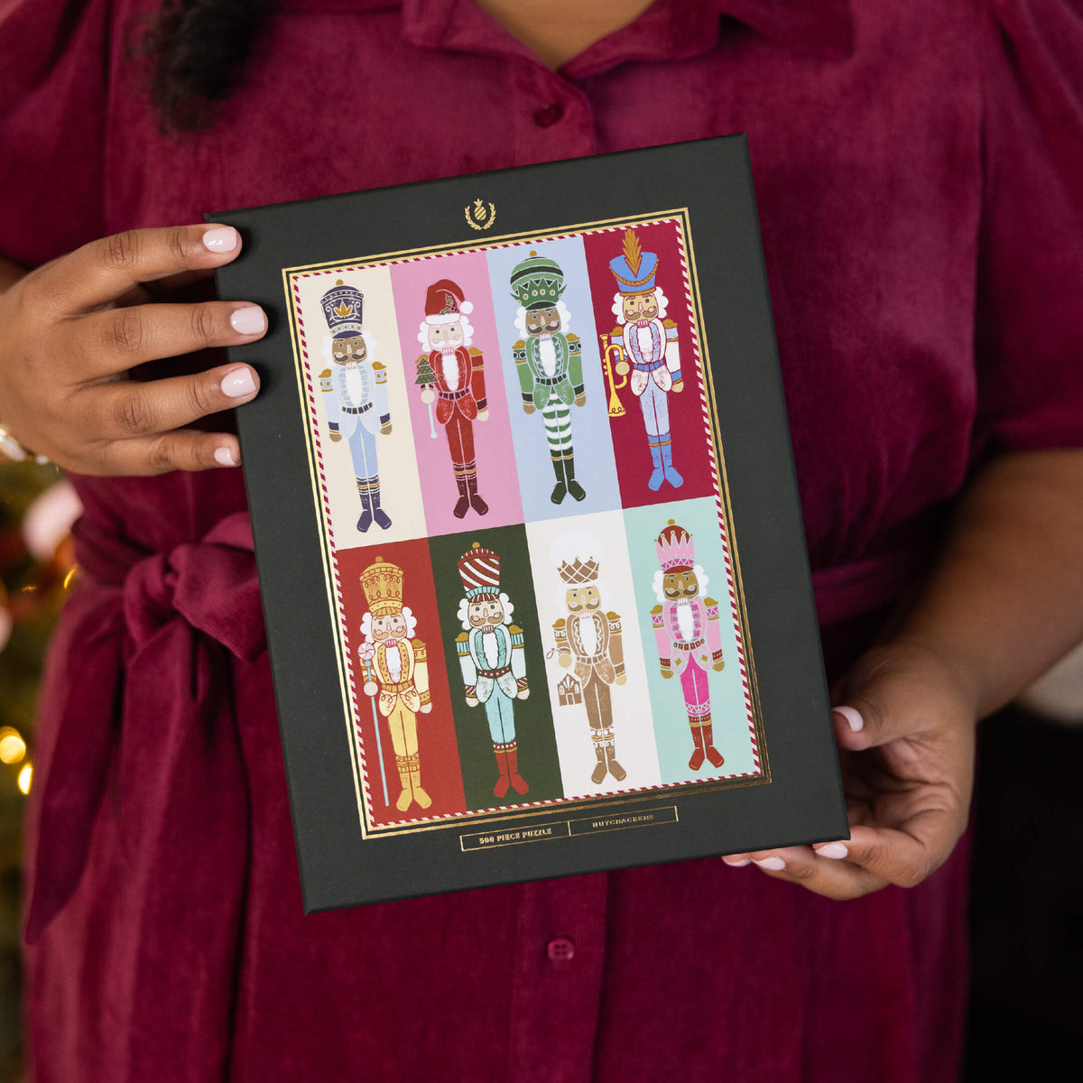 Nutcrackers 500-Piece Jigsaw Puzzle box with gold foil details, held against a burgundy dress