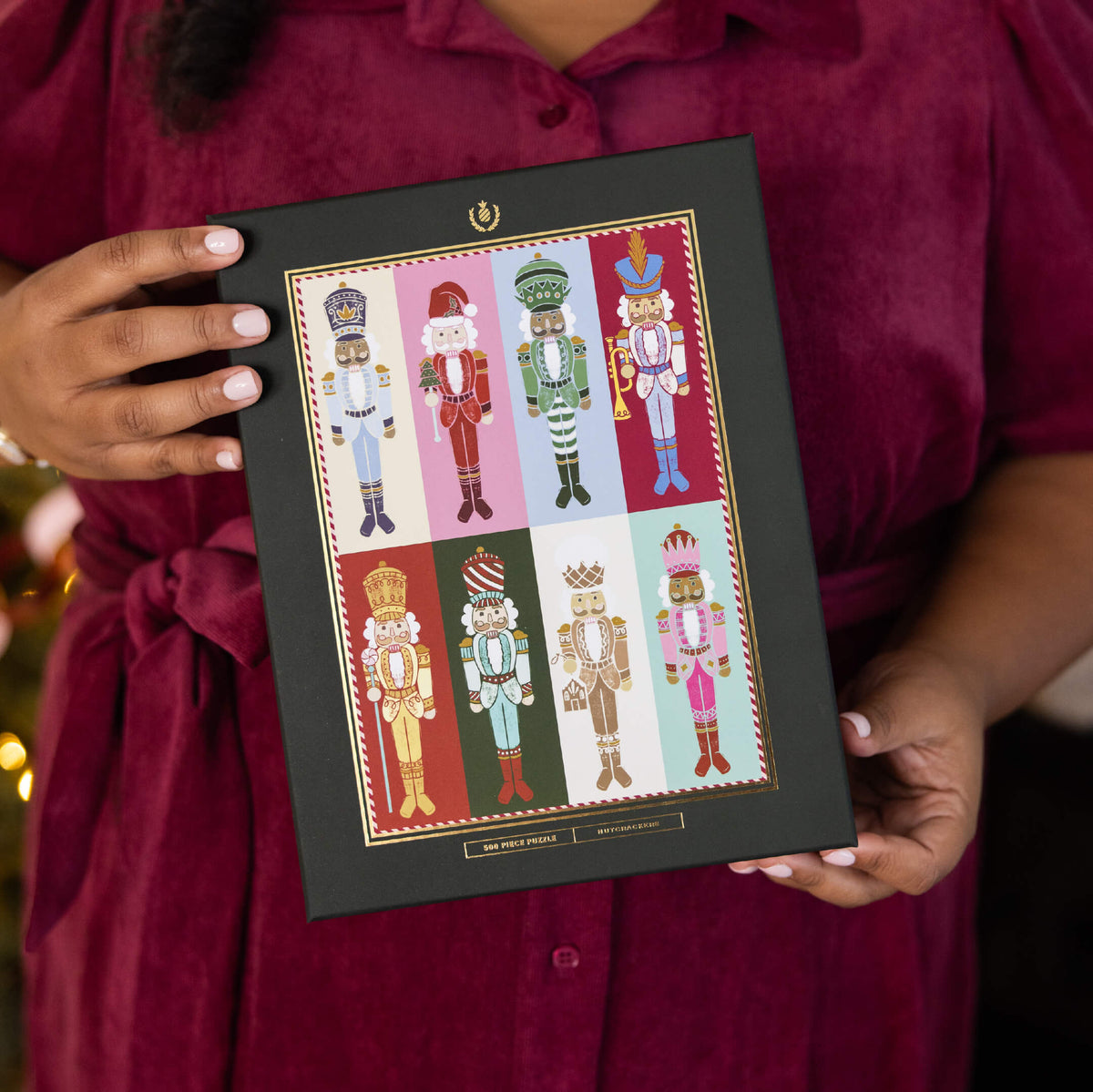 Nutcrackers 500-Piece Jigsaw Puzzle box with gold foil details, held against a burgundy dress