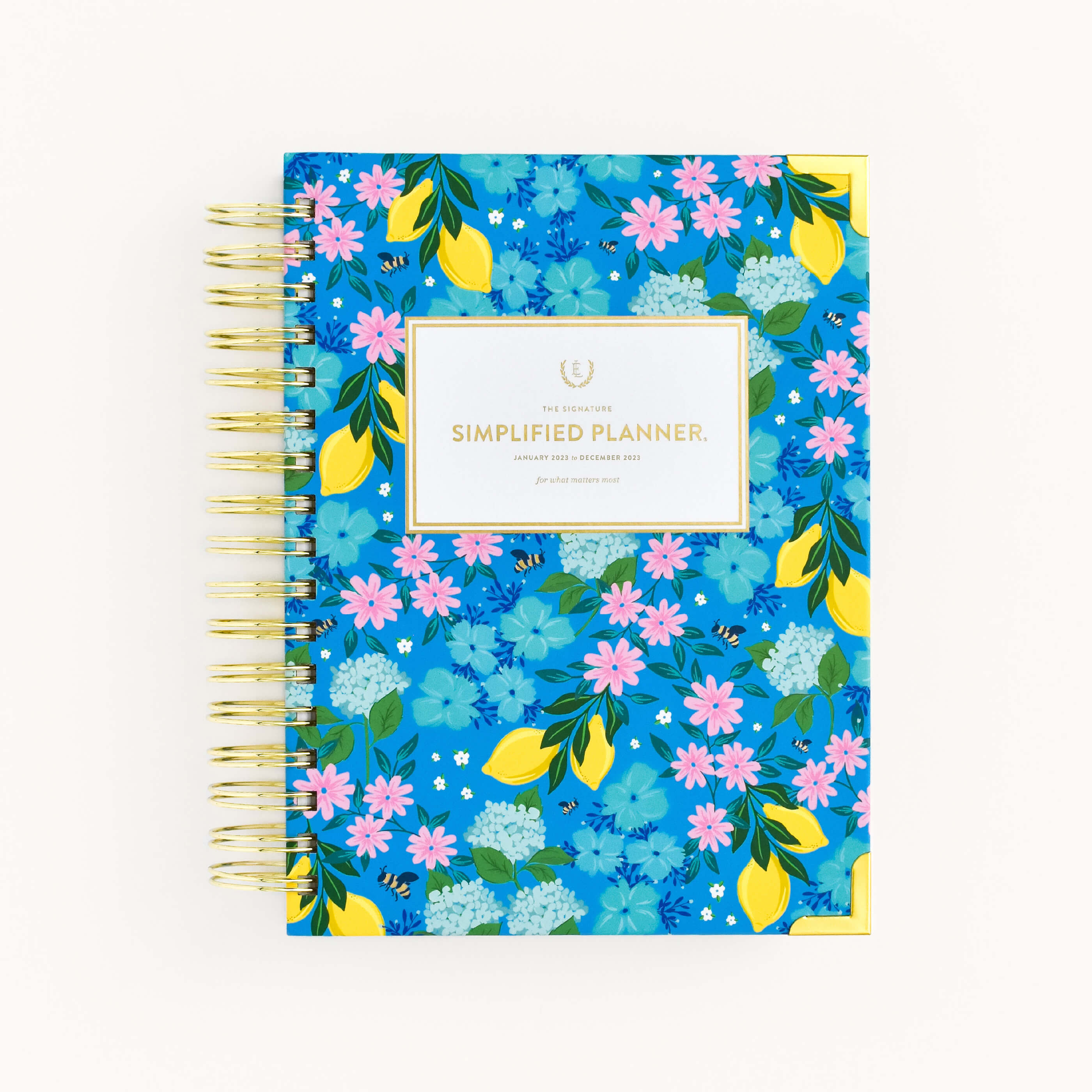 The WS - 2023 Daily, Simplified Planner, Bees In Bloom by Simplified® by Emily Ley is a spiral-bound planner with a vibrant blue cover featuring yellow lemons, colorful flowers, and a gold-accented "Simplified Planner" label at the center.