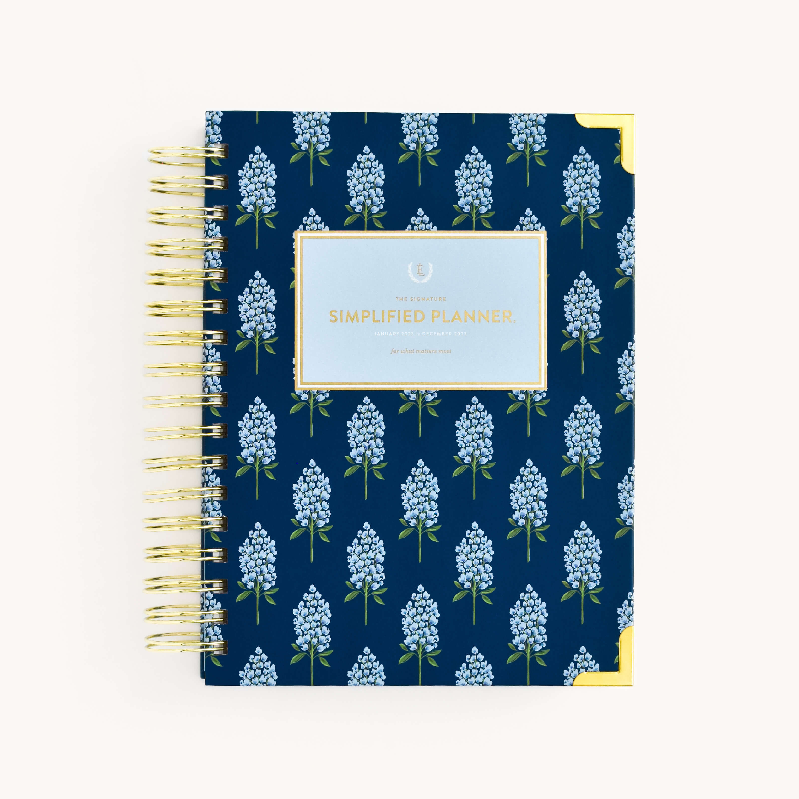 The WS - 2023 Daily, Simplified Planner by Simplified® by Emily Ley features a navy bluebonnet floral cover with gold corner accents and “Simplified Planner” in gold on a light blue label.