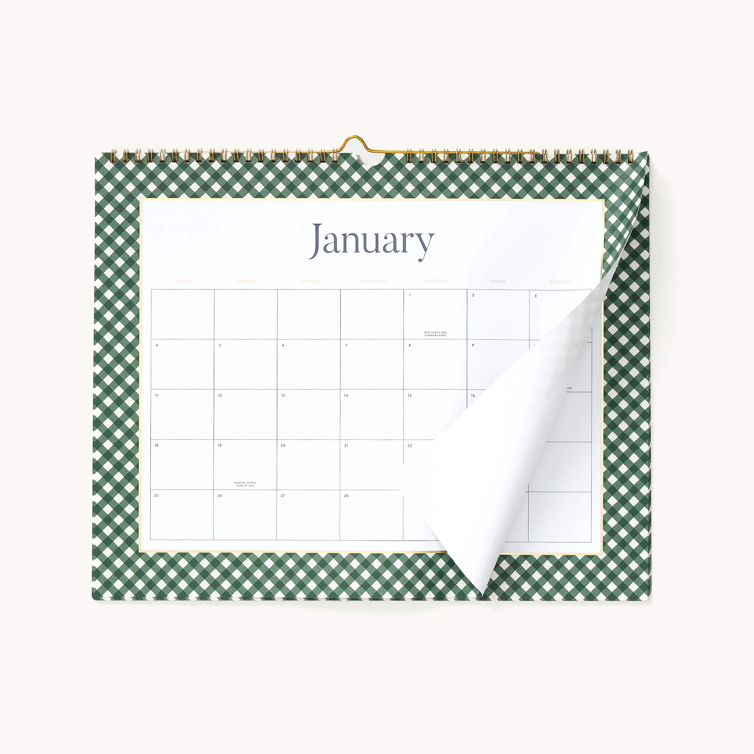 The 2026 Wall Calendar by Simplified features a green and white checkered border and is displayed open to January, with a partially turned page showing the next month beneath, hung on a white wall.