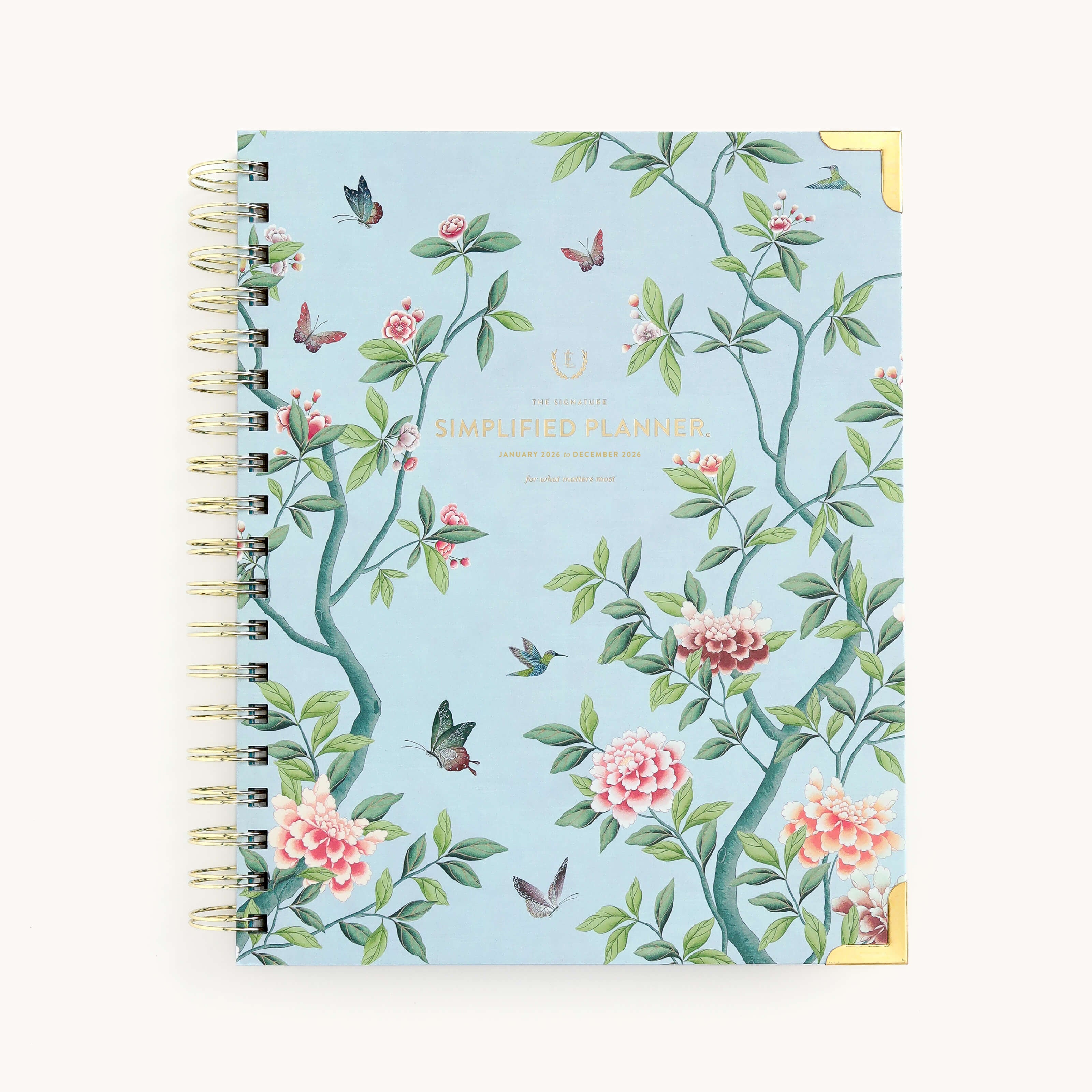 The 2026 Spiral Weekly Simplified Planner - Faraway Land by Simplified features gold corner accents, a blue cover with branches, pink flowers, and hummingbirds, plus Simplified Planner in gold—perfect for organizing your 2026 year.