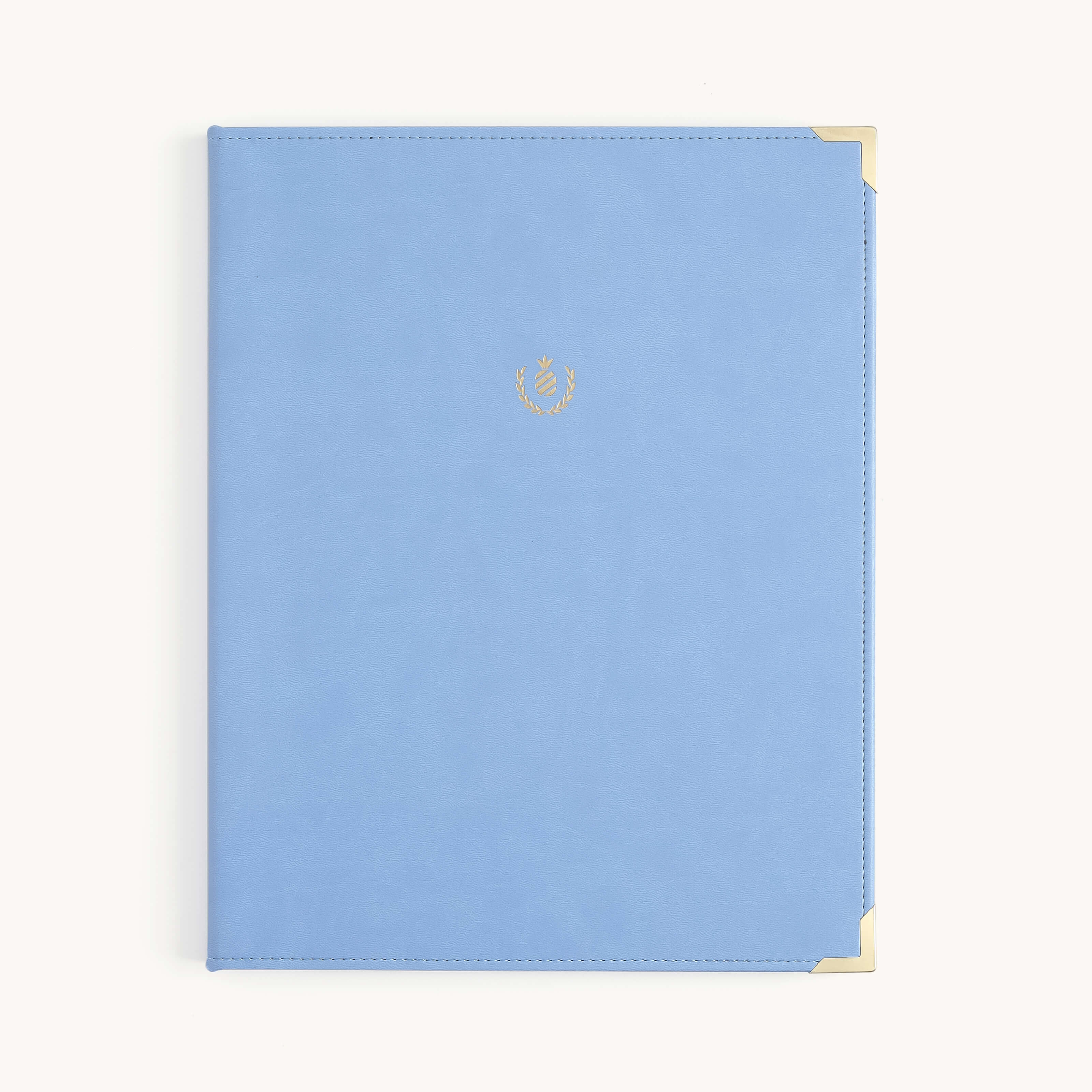 The Simplified Leatherette Folio - French Blue features a leatherette cover, gold metal corners, and a small gold laurel crest in the center, displayed on a plain light background.