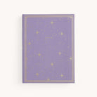 The Simplified Linen Journal - Celestial features a lavender cover with gold stars, dots, and DREAM at the center, plus a gold border. The hardcover journal is set against a plain off-white background.