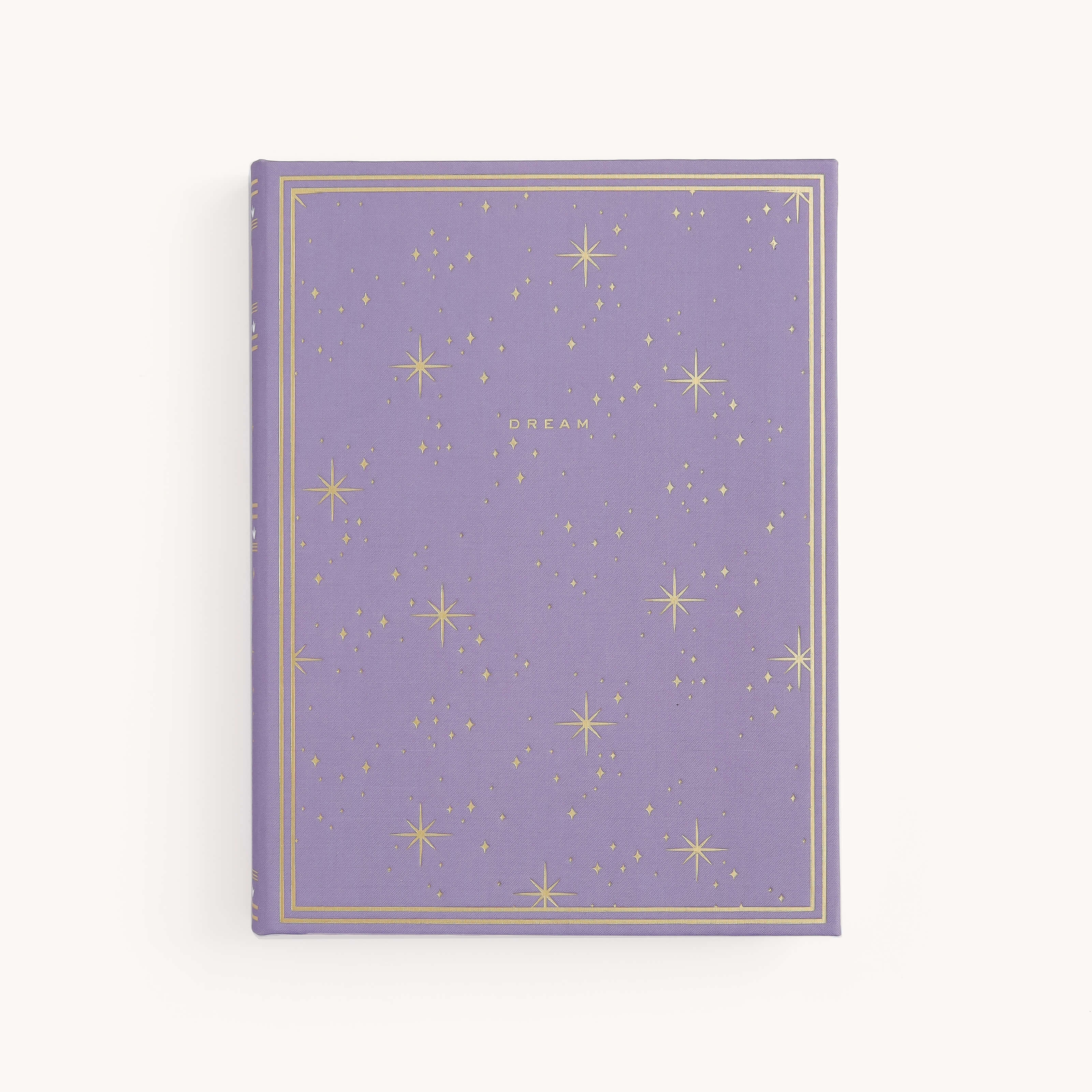 The Simplified Linen Journal - Celestial features a lavender cover with gold stars, dots, and DREAM at the center, plus a gold border. The hardcover journal is set against a plain off-white background.