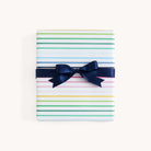 The Simplified Gift Wrap Roll - Happy Stripe features white paper with colorful horizontal stripes and gold foil accents, finished with a dark blue ribbon—an ideal choice for holiday gifts.
