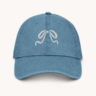 The Simplified Denim Hat - Embroidered Bow is a light blue, pigment-dyed cotton hat featuring a white embroidered ribbon bow design on the front.