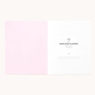 An open 2026 Softcover Monthly Simplified Planner - Happy Stripe by Simplified shows a pink left page and a white right page titled Simplified Planner, with organized, lined spaces for name and date in a minimal, clean layout.