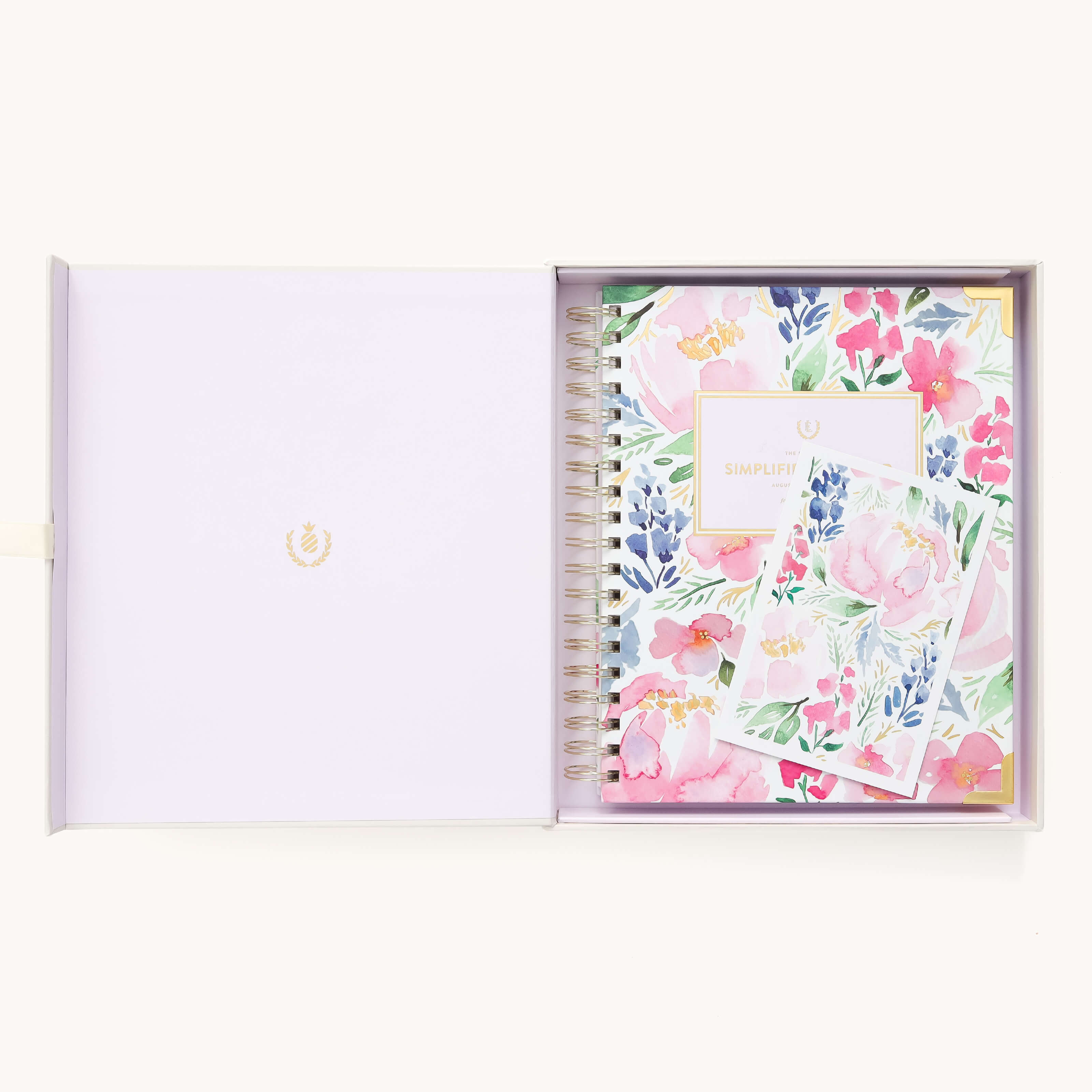 An open gift box reveals the 2026 Spiral Weekly Simplified Planner - Cottage Floral by Simplified, two matching floral notecards, and a lavender interior with a gold emblem on the left side.