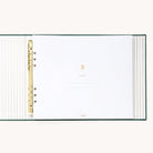 Evergreen Holiday Memories Book open to the Belongs To cover page, with a gold foil striped liner and gold o-ring binder