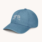 The Simplified Denim Hat - Embroidered Bow is a light blue pigment-dyed cap with a white embroidered bow on the front, displayed on a plain off-white background.