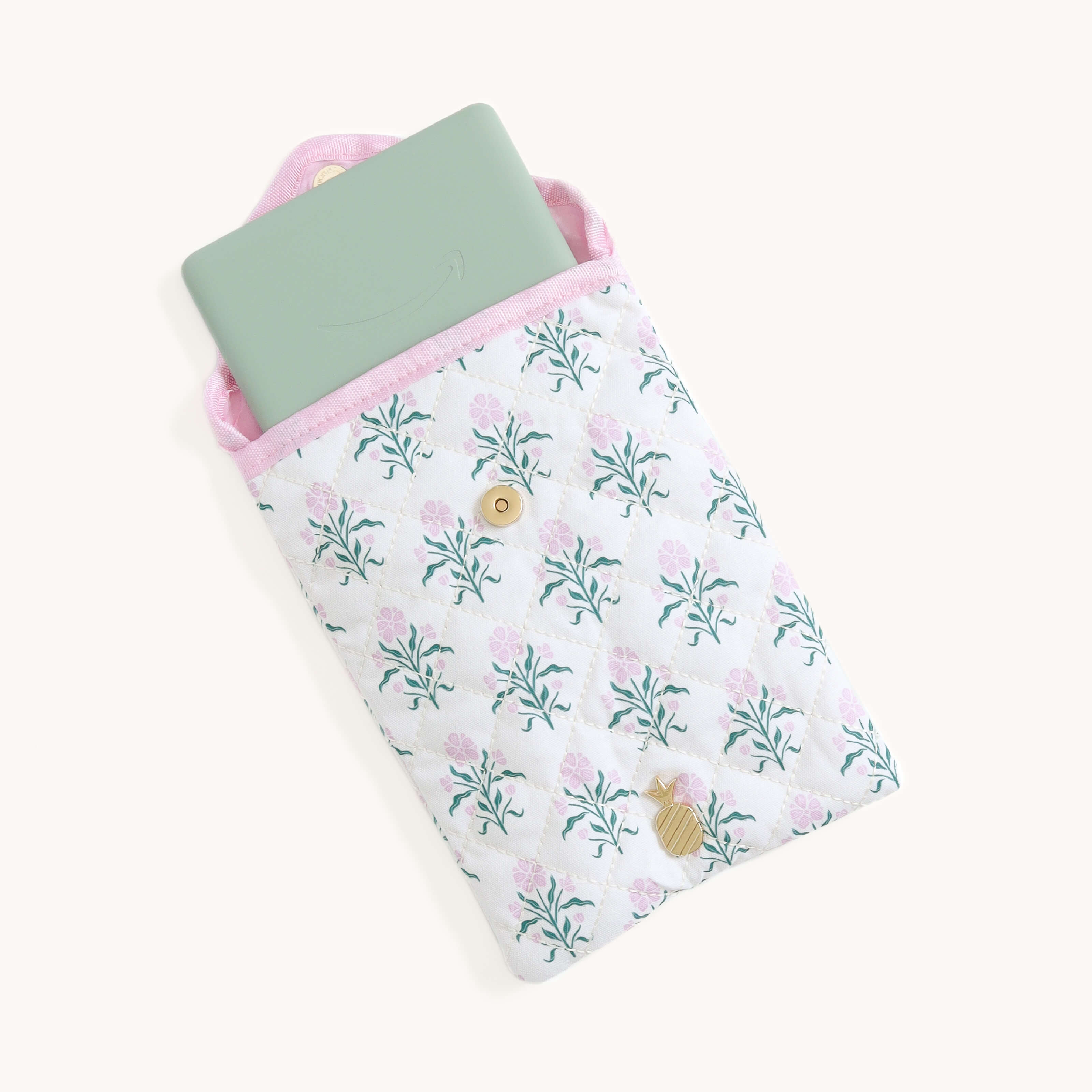 Floral patterned Blush Botanical Quilted E-Reader Case with an e-reader inside with a gold pineapple charm on a white background
