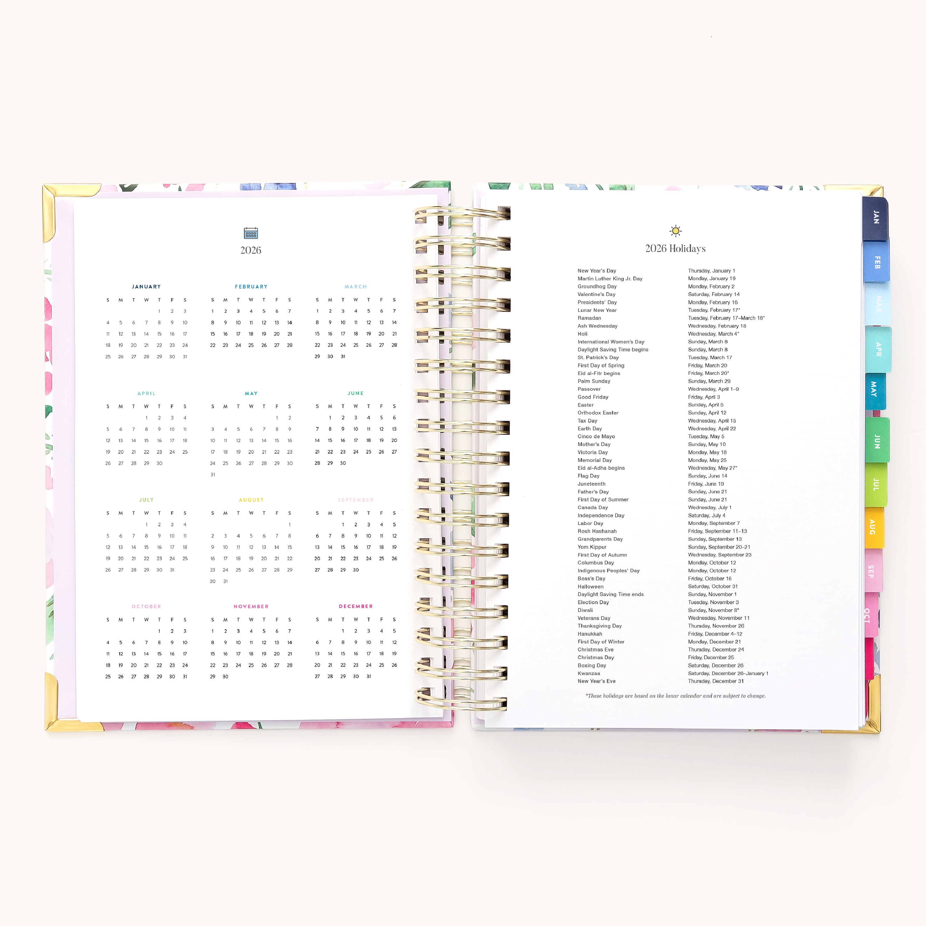The Simplified 2026 Spiral Daily Simplified Planner - Cottage Floral features gold spiral binding and colorful tabbed sections, with a 2026 calendar on the left page and a list of 2026 holidays on the right.