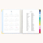 The 2026 Spiral Weekly Simplified Planner - Serene Stripe by Simplified features a yearly calendar on the left and holidays list on the right, with color-coded tab dividers along the edge for easy weekly planning.