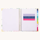 The 2025-2026 Spiral Weekly Simplified Planner - Cottage Floral by Simplified features a minimalist design with white pages and gold foil details. It includes colorful, labeled section tabs and a clear pocket holding a ruler and sticky tabs in various colors for easy prep work.