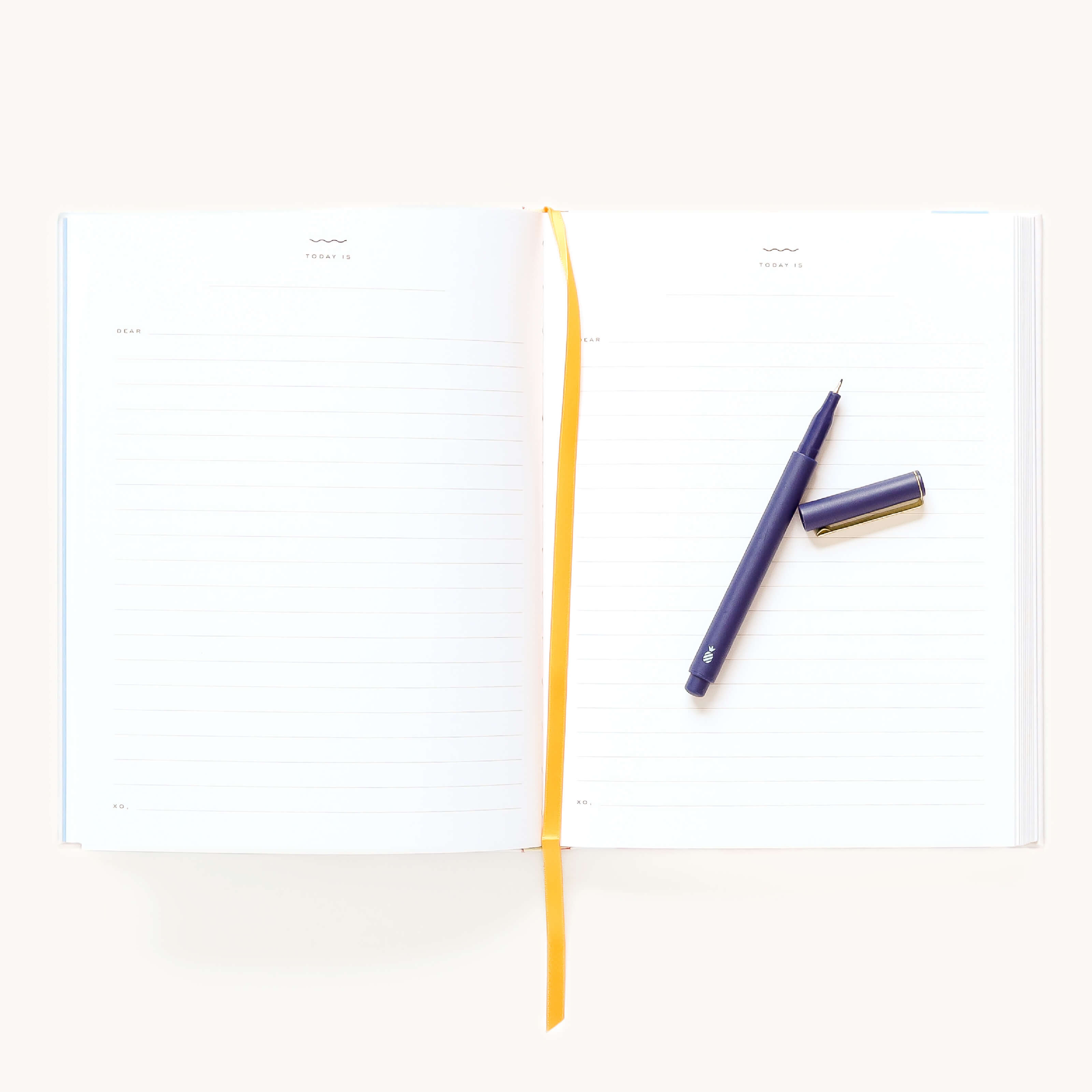 The Simplified Linen Journal - Back and Forth, with lined pages and a yellow ribbon bookmark, lies open on a plain white background. A black pen with its cap off rests on the right page, ready for your thoughts.