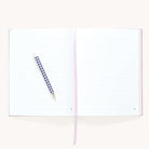 The Simplified Linen Journal - Celestial features open lined pages, a blue and white checkered pen on the left page, and a light purple ribbon bookmark across the center.