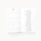 The 2026 Bookbound Daily Dapperdesk Planner - Carolina Dot by Simplified features a 12-month spread with a yearly calendar on the left and holidays and observances listed by date on the right, all in small black text on crisp white paper.