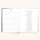 The Simplified 2026 Bookbound Weekly Dapperdesk Planner in Evergreen features a leatherette cover, with a yearly calendar on the left and holidays on the right, both in black text on crisp white pages.