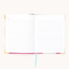 The Simplified 2026 Bookbound Weekly Simplified Planner – Happy Stripe features lay-flat binding, lined pages, and a light blue ribbon bookmark, with Notes labeled on the top left page, ready for writing on a white background.
