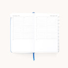 The Simplified 2026 Bookbound Daily Dapperdesk Planner - Carolina Dot is shown open to January 4–5, displaying hourly slots, checkboxes, a notes section, a blue ribbon bookmark, and right-side tabs.