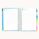 An open 2026 Spiral Daily Simplified Planner – Faraway Land by Simplified displays two daily pages with time slots from 6 a.m. to 7 p.m., notes sections, colorful side tabs, and a charming hand-painted pattern.