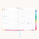 An open 2026 Bookbound Weekly Simplified Planner - Happy Stripe by Simplified, featuring a lay-flat binding, weekly layout with lined daily sections (Jan 7–13, 2026), and colorful index tabs along the right edge.