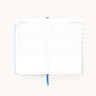 The 2026 Bookbound Daily Dapperdesk Planner - Carolina Dot by Simplified features lined pages for scheduling from 7 a.m. to 8 p.m., note sections, tabbed right pages, a blue ribbon bookmark, and a stylish leatherette cover.