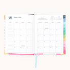 The 2026 Bookbound Weekly Simplified Planner - Happy Stripe by Simplified shows a January monthly spread with colorful tabs, note sections, blank days except for New Year’s Day, and lay-flat binding for easy writing.