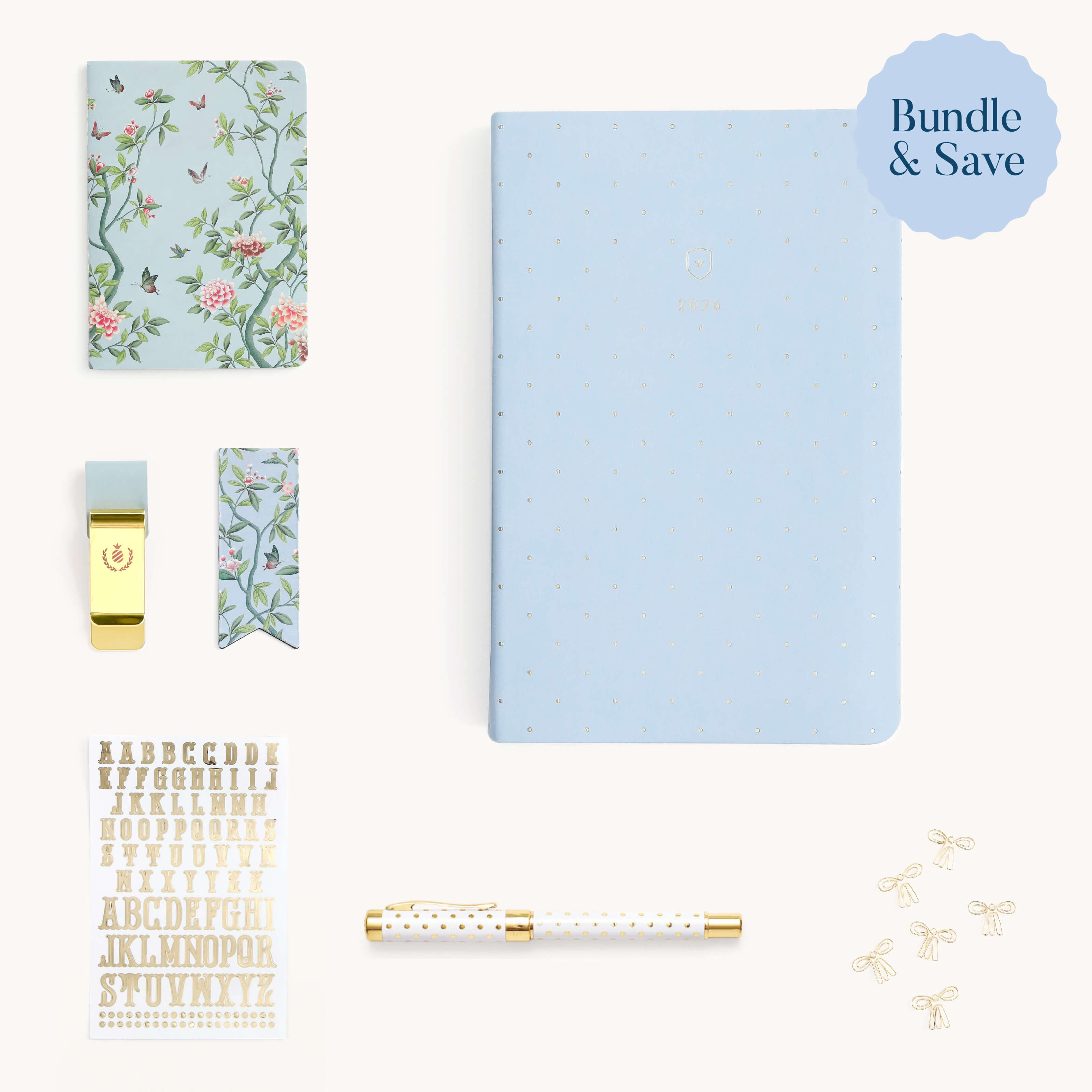 Flat lay of the Daily Dapperdesk Ultimate Bundle by Simplified® featuring a blue polka dot notebook, floral notepad, gold clip, ribbon bookmark, gold stickers, chic pen, and small bows. “Bundle & Save” label in corner.