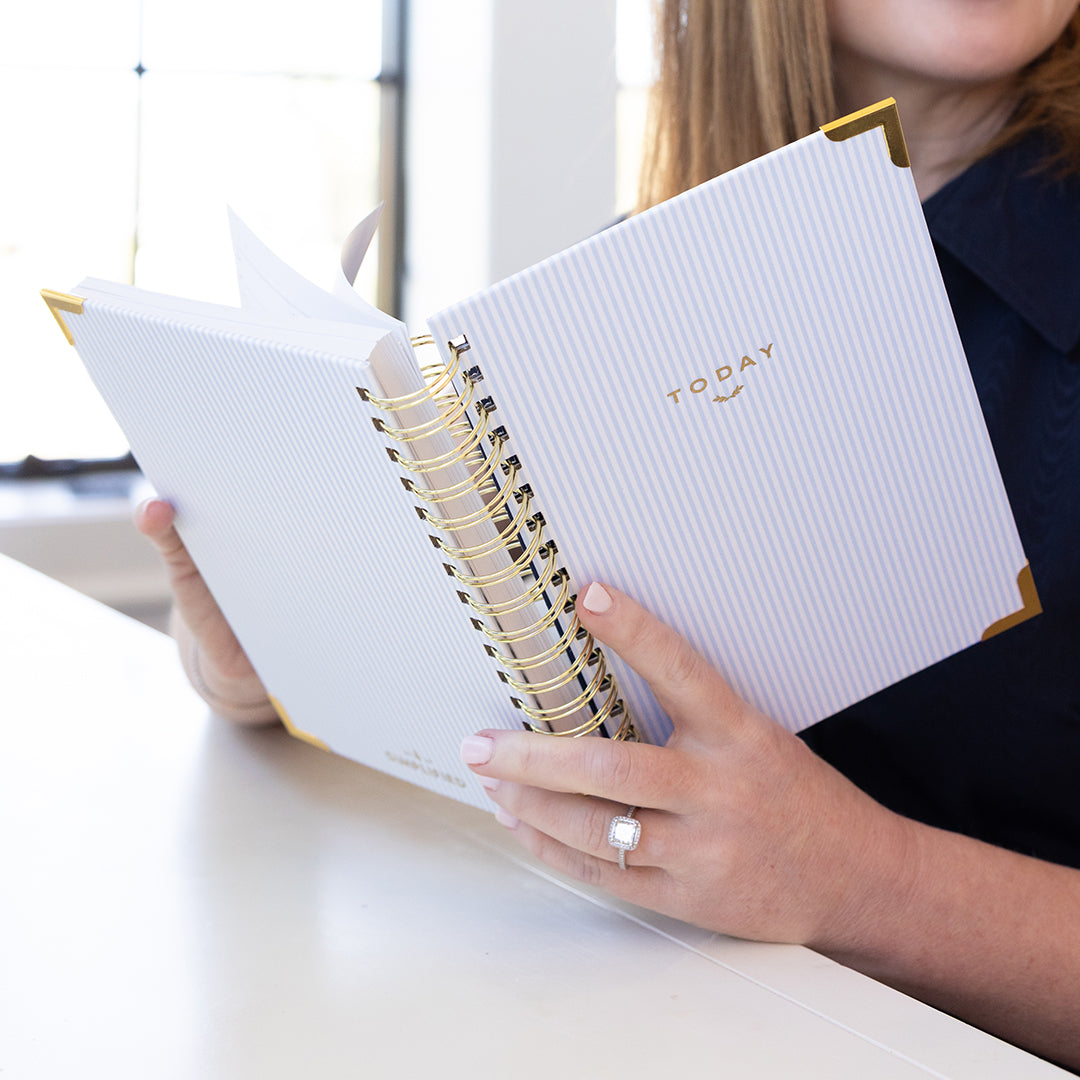 spiral daily planner styled in use with blue pinstripe cover and gold accents for a clean, elegant daily planning routine