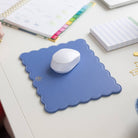 A white wireless mouse sits on the Simplified Scalloped Mousepad in French Blue, accompanied by a planner, striped notepad, and gold paperclips.