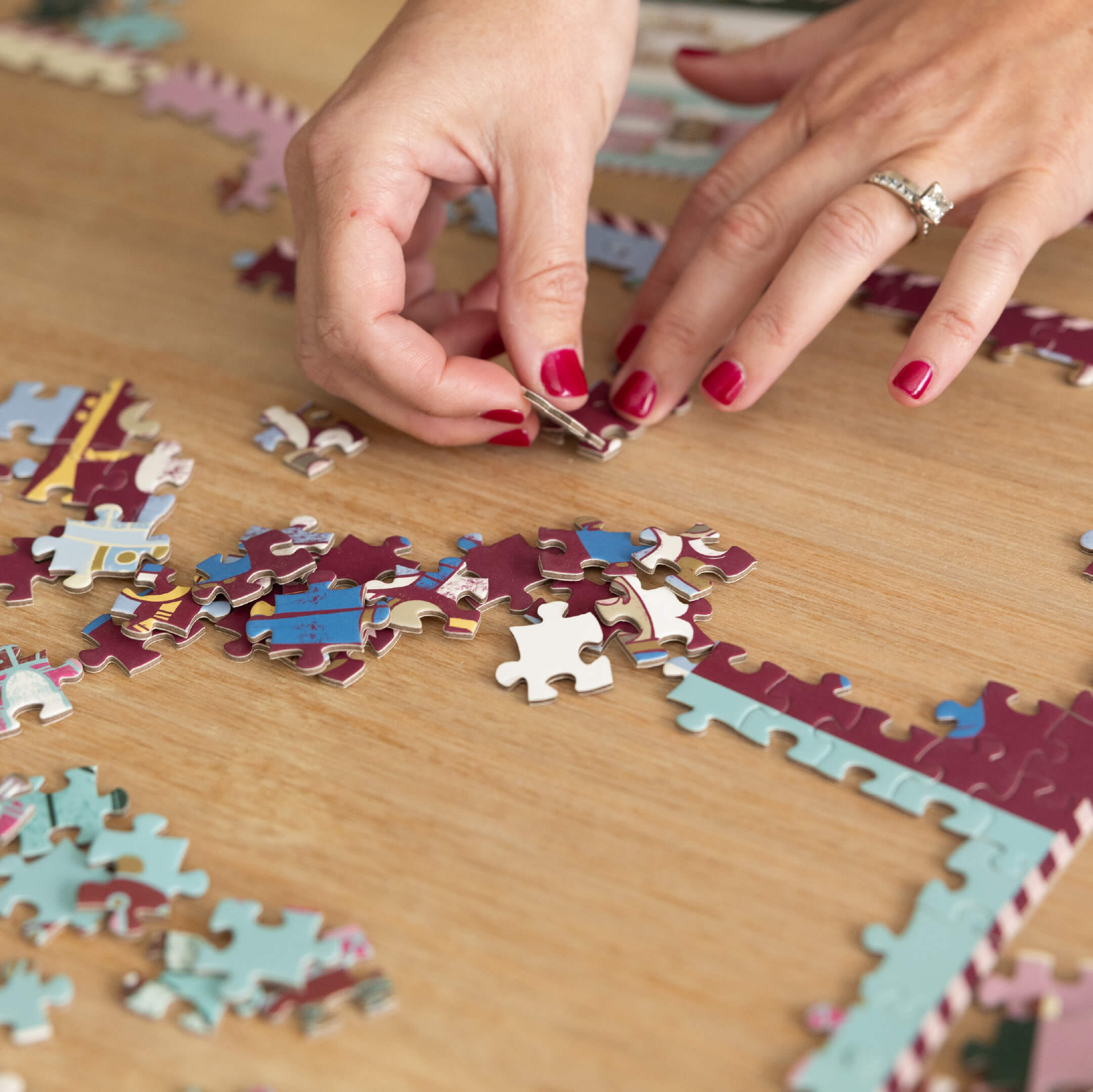 Nutcrackers 500-Piece Jigsaw Puzzle in progress on a wood table, with hands fitting together the border pieces