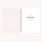 An open spiral-bound Workbook - Faith by Simplified, featuring a pink and white checkered inside cover on the left and a title page on the right with space for a name, designed for goal-setting and making actionable plans.