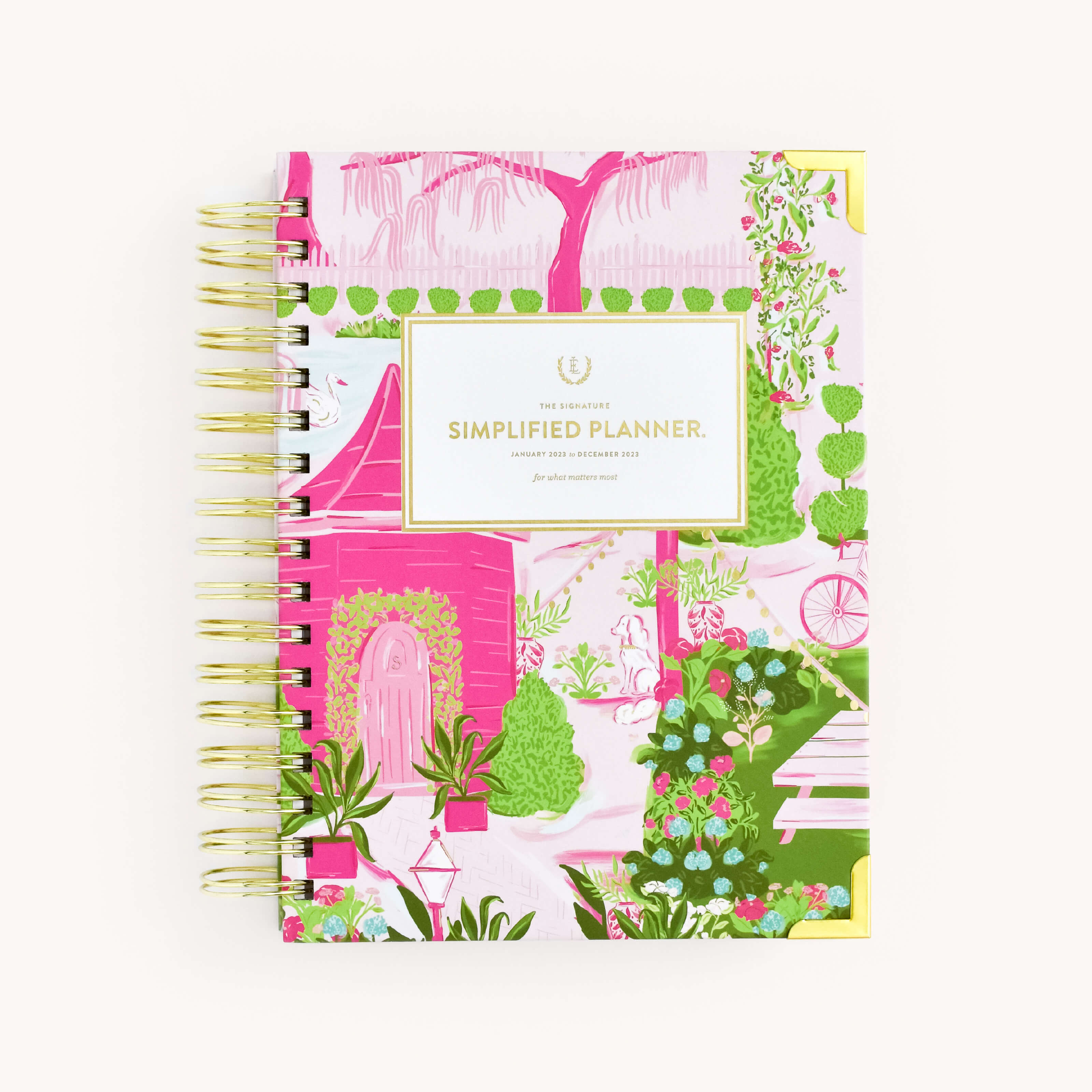 The WS - 2023 Daily, Simplified Planner, Charlotte Street by Simplified® by Emily Ley is spiral-bound with a colorful cover of pink, green, and white trees, plants, and a cottage. The label reads The Signature Simplified Planner with gold accents.
